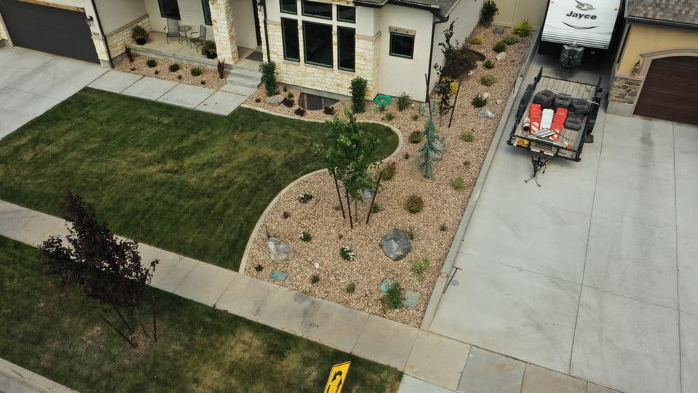 Aerial view of a landscaped home exterior with gravel, plants, and a parked trailer.